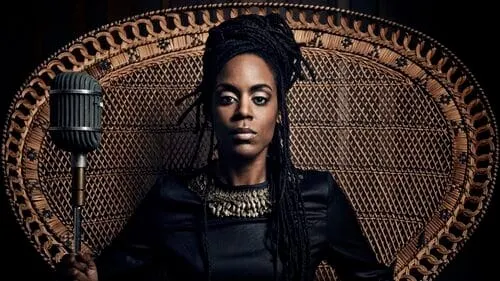 Microphone in front of a woman with dreadlocks sitting on an ornate chair, dark background, confident expression, music or po