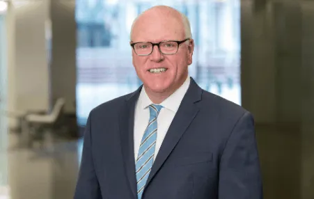 CEO in professional business suit smiling at the camera in modern corporate office environment.
