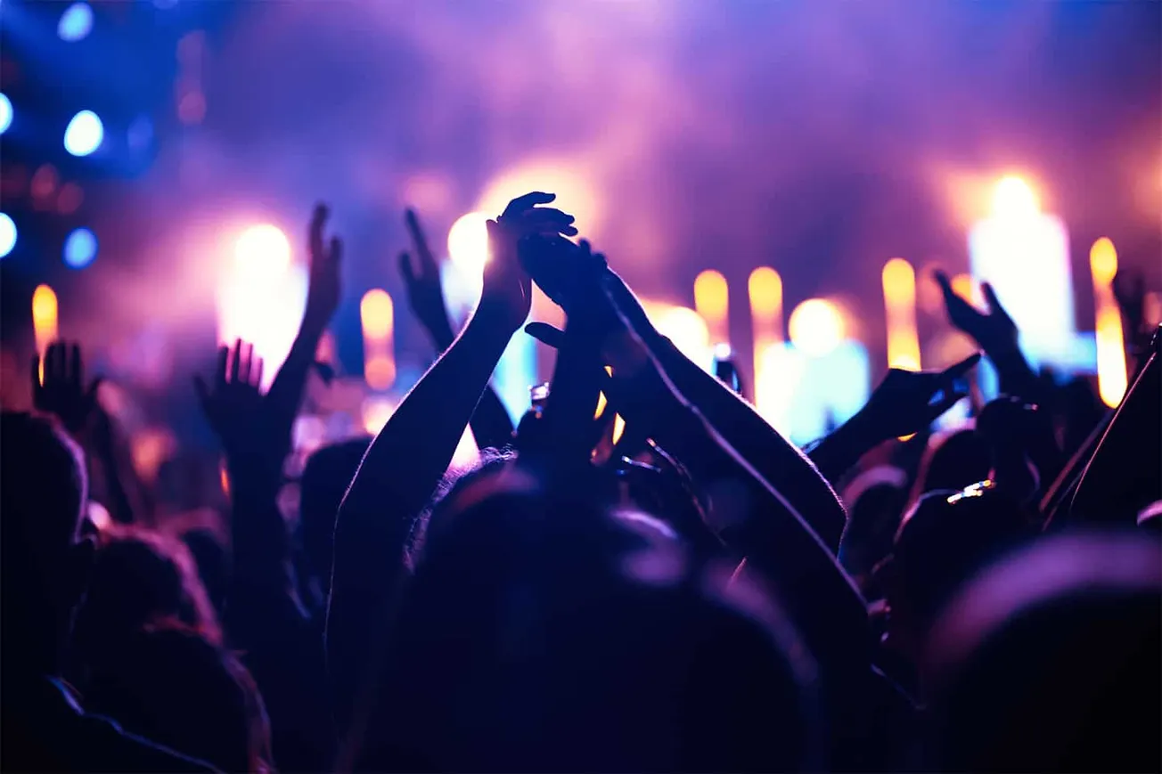 Vibrant concert crowd dancing and raising hands in a music festival with colorful stage lights and lively atmosphere, represe