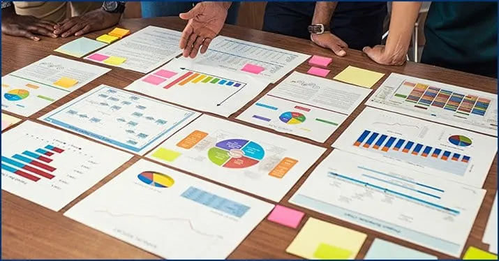 - Various business charts and graphs printed on paper spread across a wooden table, with people analyzing data and discussing