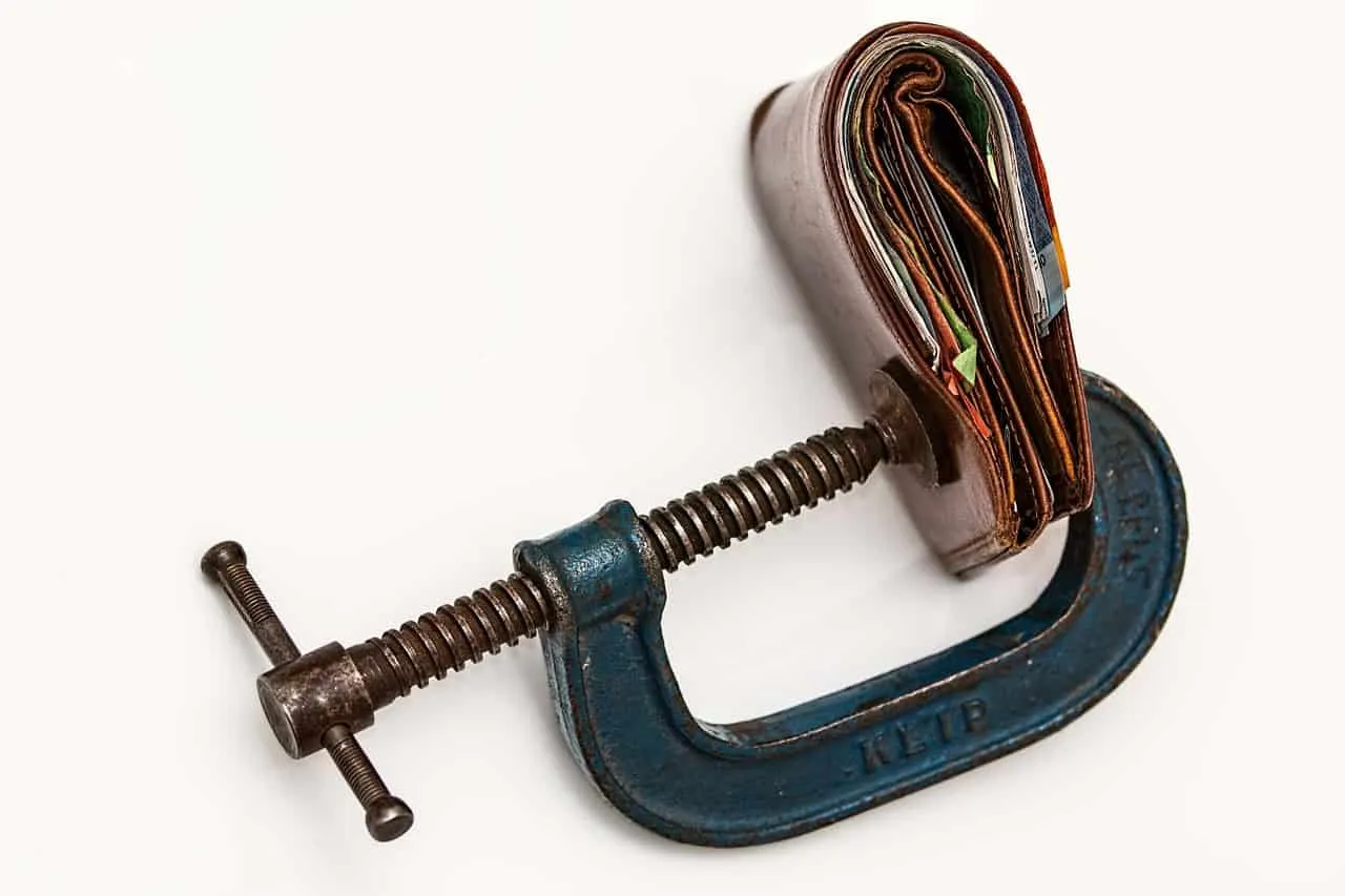 Clamped wallet with money using a C-clamp, symbolizing financial pressure or budget constraints.
