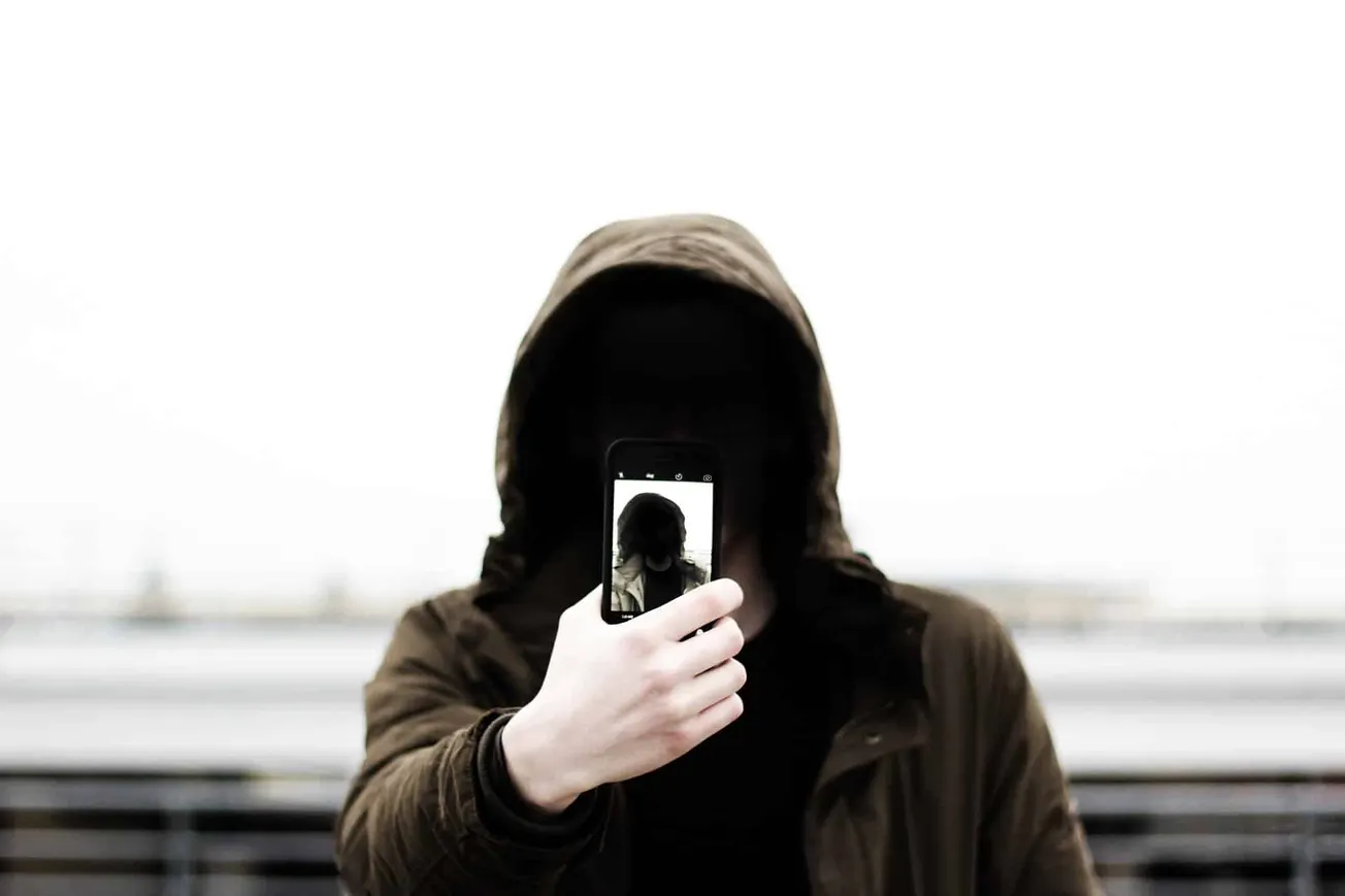 Hypebot music industry news, persona, and digital marketing concepts, person taking photo in hoodie with smartphone on bridge