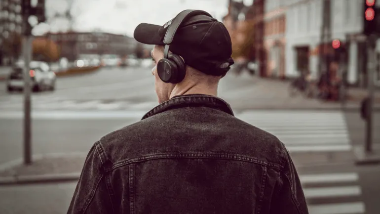 Headphones on man walking across city street, urban environment, music or podcast listening, street scene, trendy city lifest