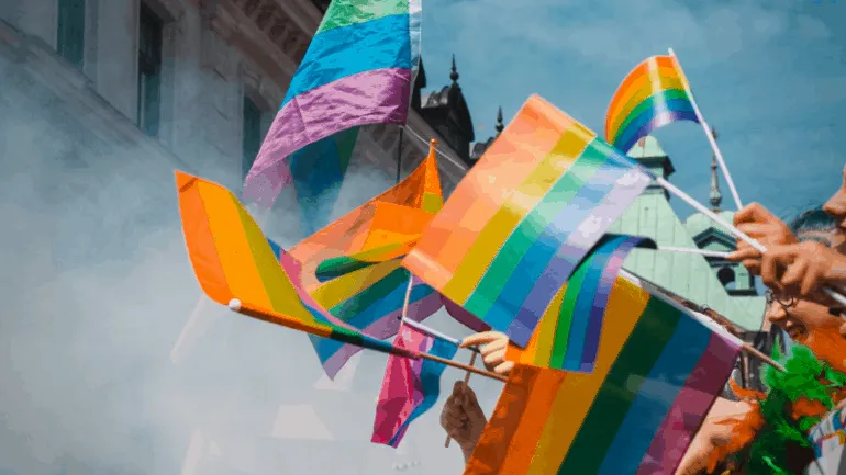 Multi-colored pride flags being waved at a LGBTQ+ pride parade, symbolizing diversity and celebration.