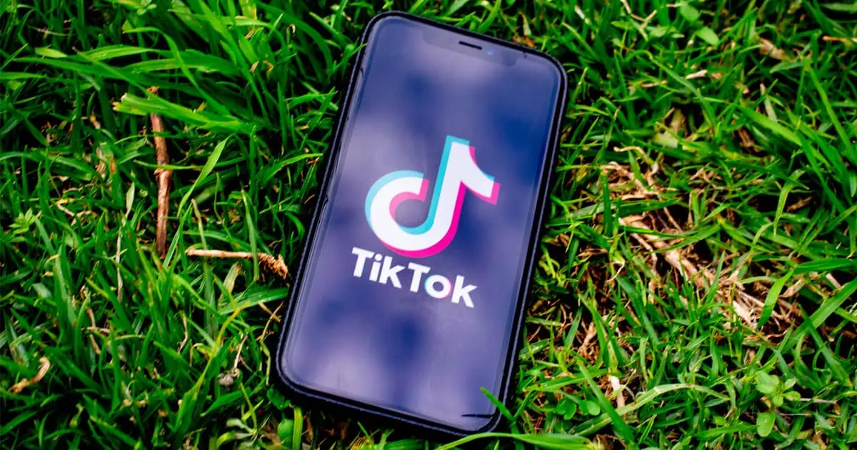 TikTok app on smartphone lying on green grass, promoting social media trends, user-generated content, viral videos, and digit