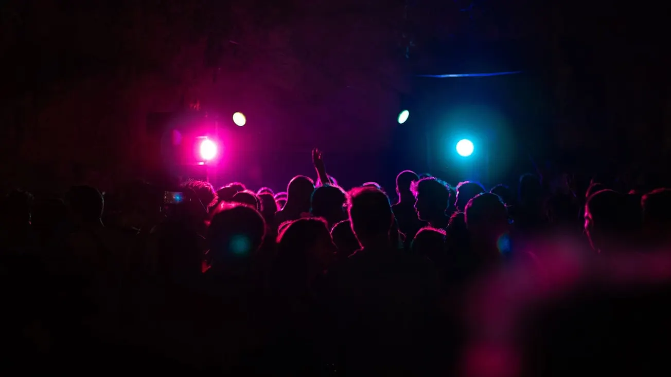 Vibrant night club scene with colorful LED stage lights illuminating a large crowd of concert attendees.