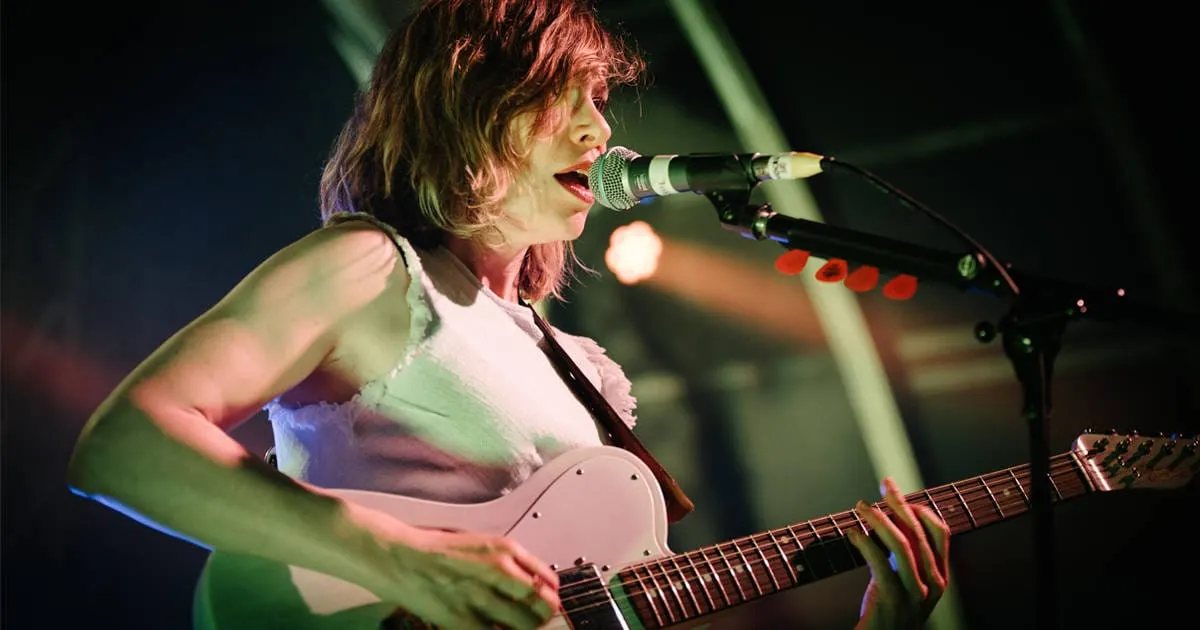 Musician performing live on stage with guitar and microphone at a music concert or festival in vibrant lighting.