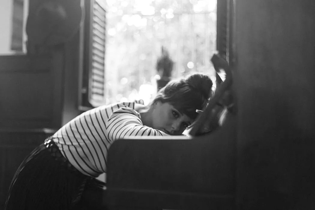 Young woman resting her head on a piano, black and white photo, indoors with natural light, capturing a moment of relaxation