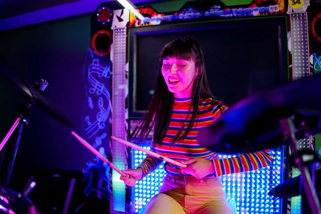 An energetic young woman playing electronic drums in a colorful music arcade with neon lights and musical notes, enjoying liv
