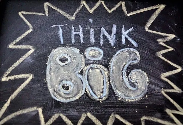 Big bold "Think Big" message written in chalk on a blackboard with decorative chalk border emphasizing motivation and success