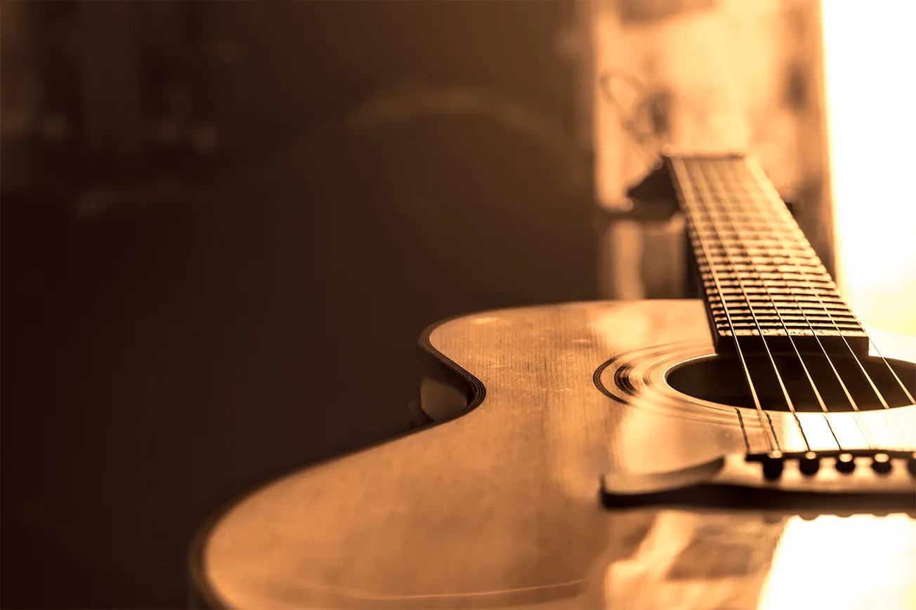 Guitar on wooden surface illuminated by warm sunlight, close-up view emphasizing strings and sound hole, music instrument use