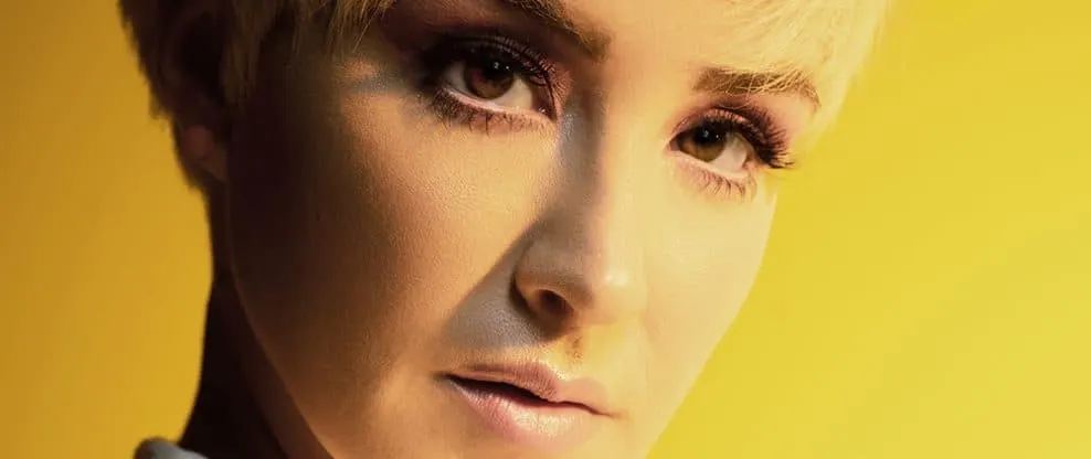 Highlights of a woman with short blonde hair and makeup, related to music and entertainment industry, vibrant yellow backgrou