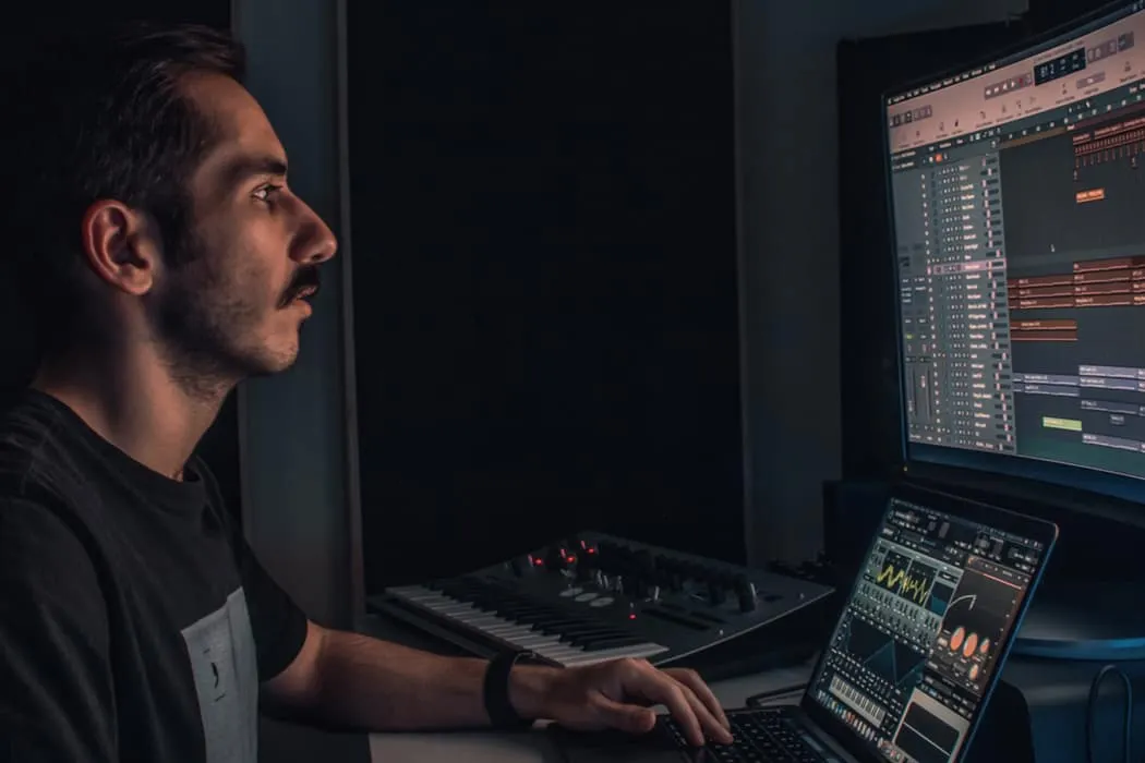 Professional music producer working on digital audio workstation with MIDI controller and synthesizer in a dark studio.