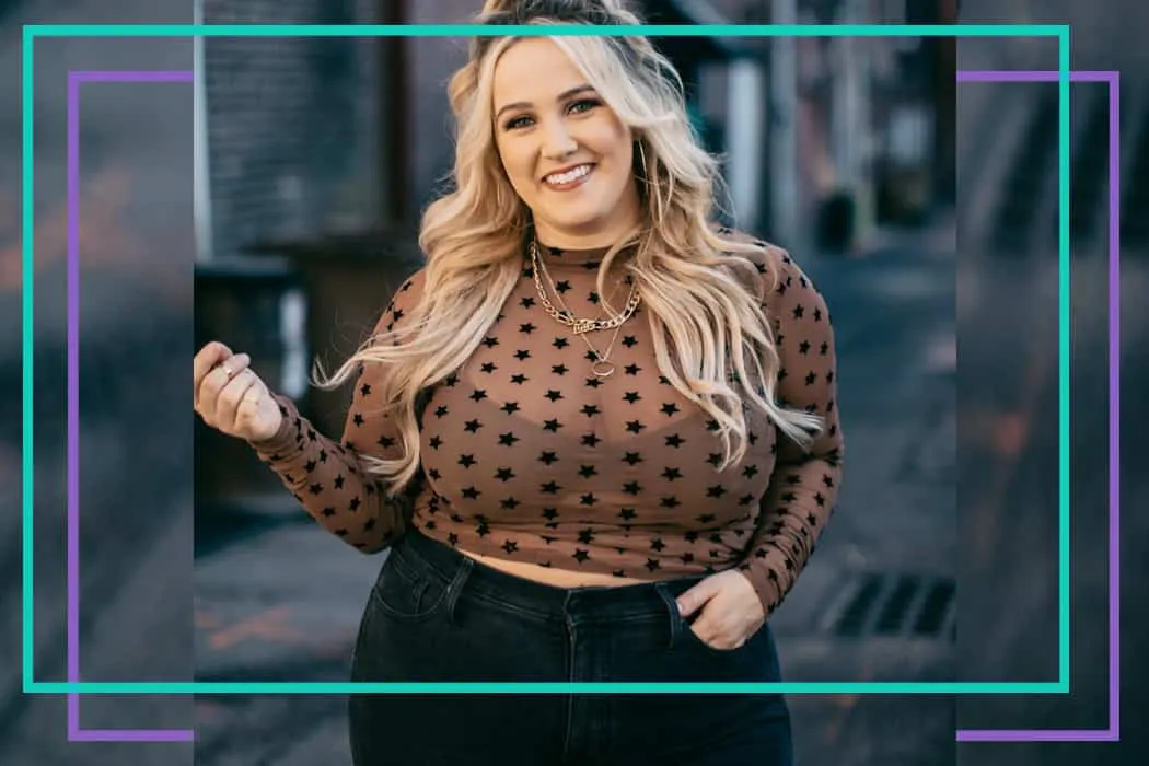 Blonde woman smiling outdoors wearing a sheer brown top with black stars, black high-waisted jeans, and layered gold necklace