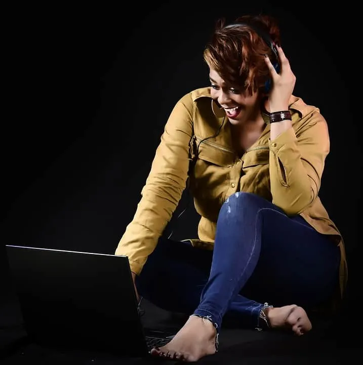 Young woman in headphones laughing while using a laptop on black background, music streaming, digital entertainment, casual h