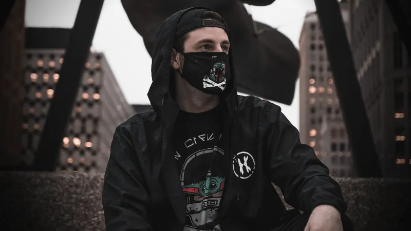 Face masked young man in urban cityscape wearing black hoodie and graphic t-shirt urban street fashion hype culture.