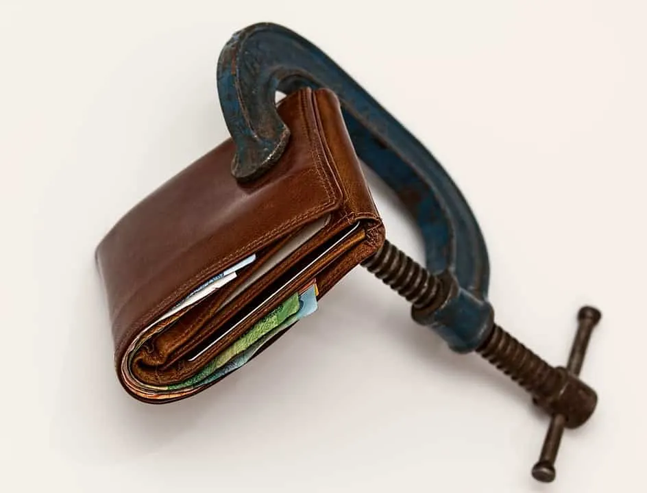 A leather wallet secured with a blue clamp, weighing down paper currency and receipts, symbolizing financial pressure and str