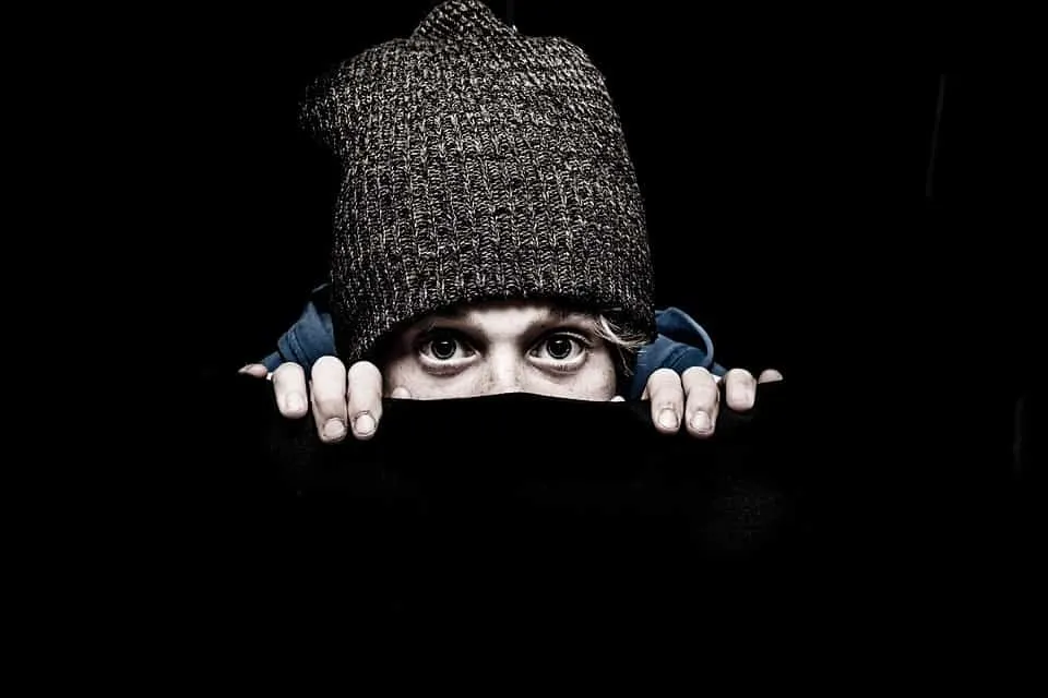 Wary young person peeking from dark background, wearing a knit beanie, emphasizing privacy and curiosity, suitable for digita
