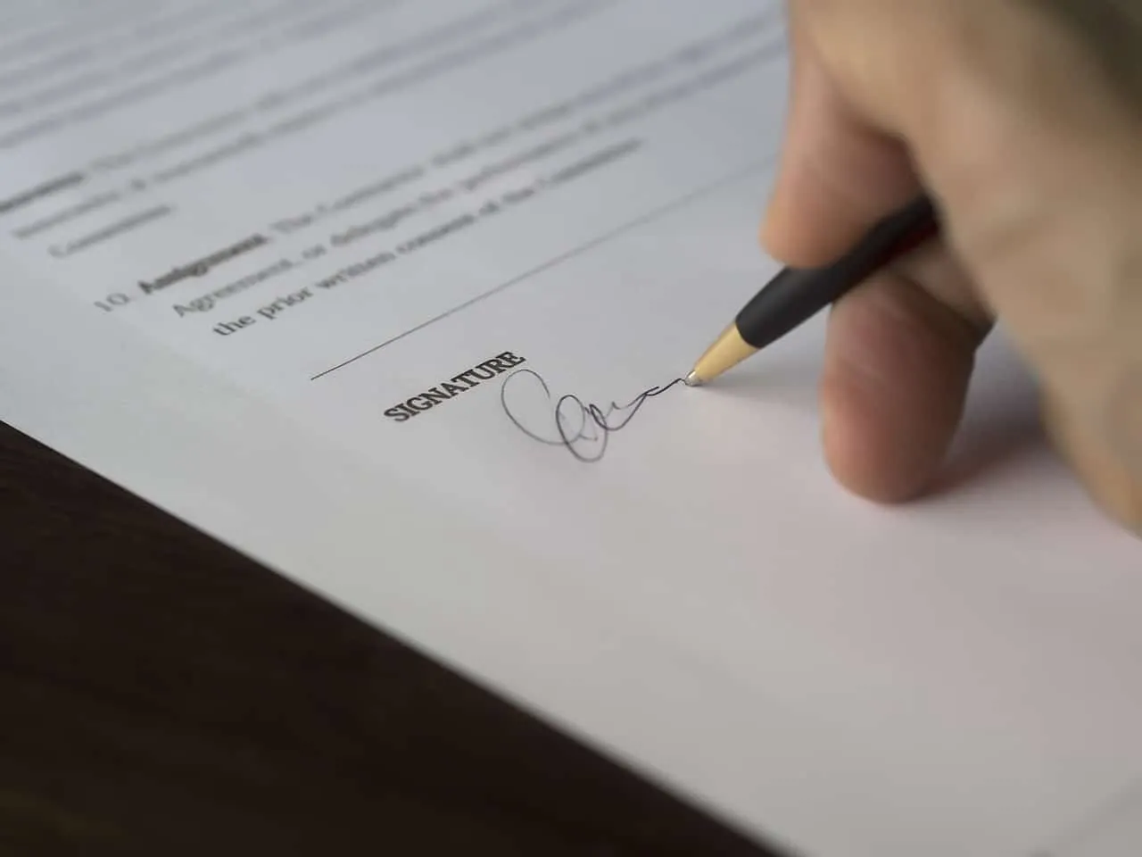 Signature being written on a document with a pen, representing legal or formal paperwork, contracts, or agreements.