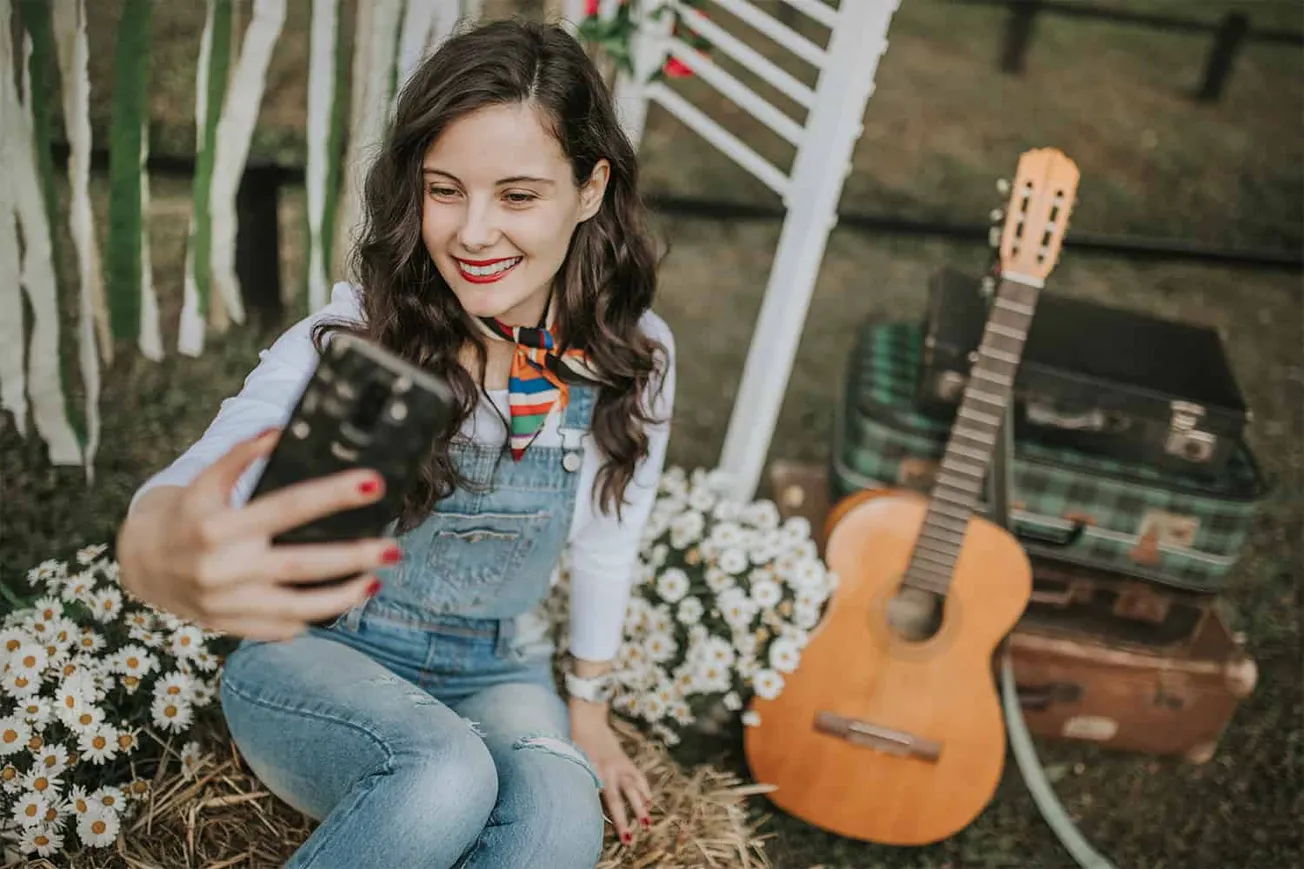 Girl taking selfie at outdoor music event with guitar and daisies, casual summer vibe, social media, live music, outdoor ente