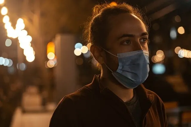 A young woman wearing a face mask in an urban setting at night, with blurred city lights in the background, highlighting COVI