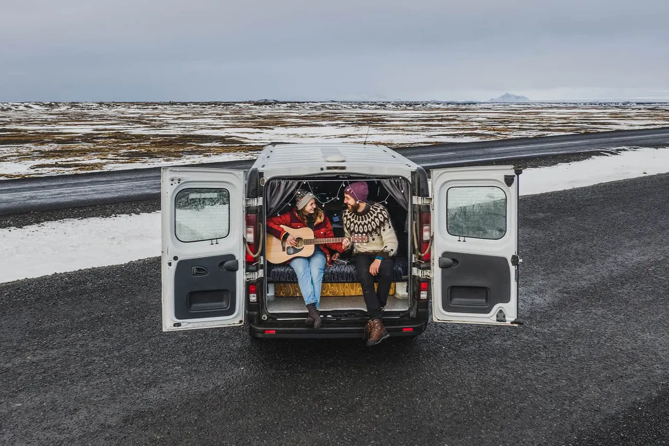 Cozy winter road trip with two friends enjoying acoustic guitar music inside a campervan in a snowy landscape. Music, travel,