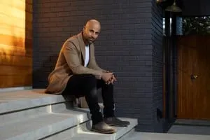 Man sitting on stairs outside modern building, urban environment, casual attire, relaxed pose.