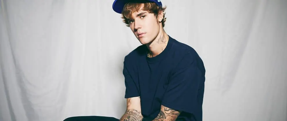 Young male musician with tattoos wearing a blue shirt and cap, studio portrait.