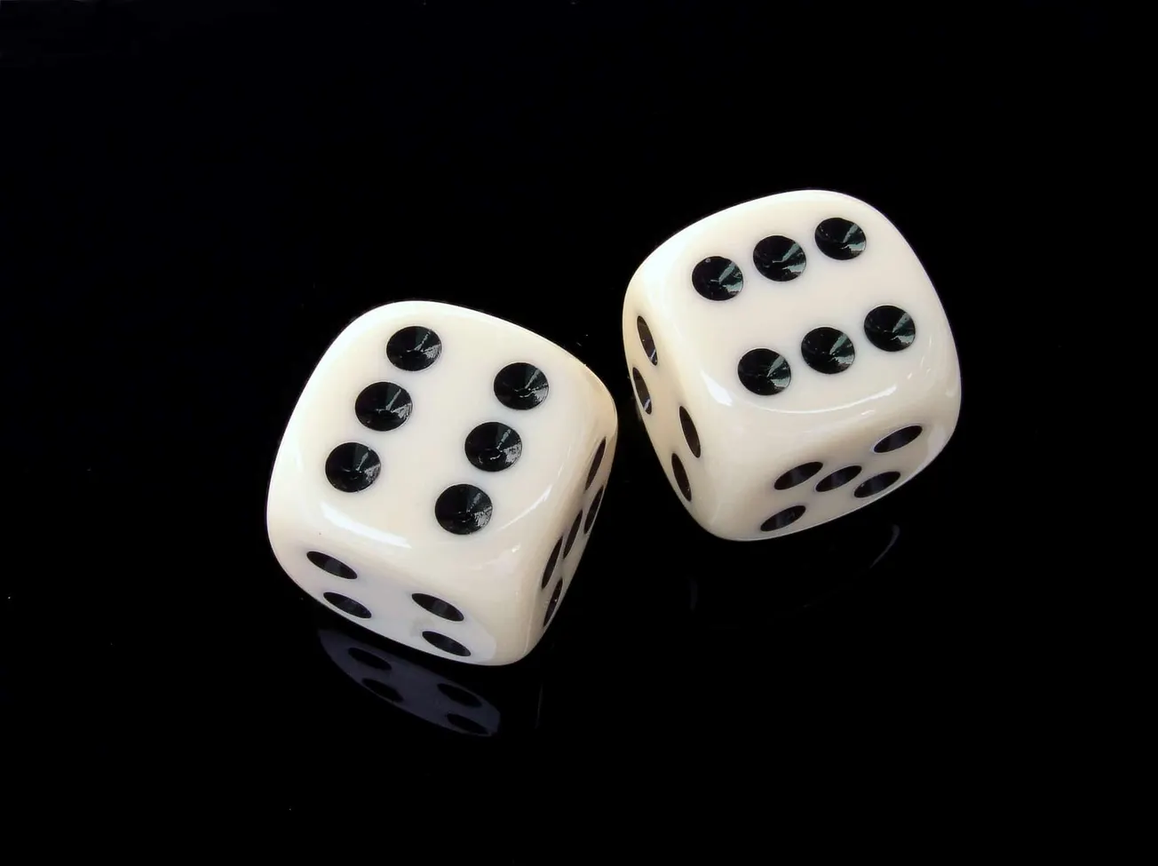White dice with black pips on a glossy black surface, illustrating chance and probability concepts.
