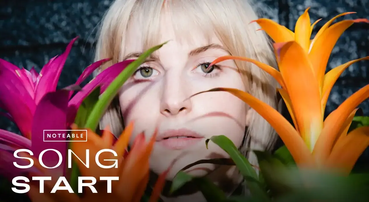 Bright blonde woman surrounded by vibrant tropical flowers, emphasizing music and pop culture themes, with a focus on fresh,