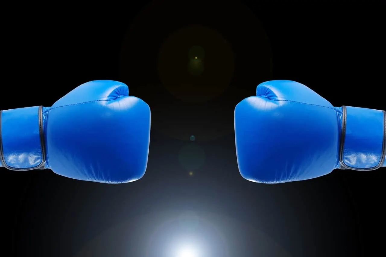 Blue boxing gloves facing each other against a black background, symbolizing competition or conflict, digital image related t