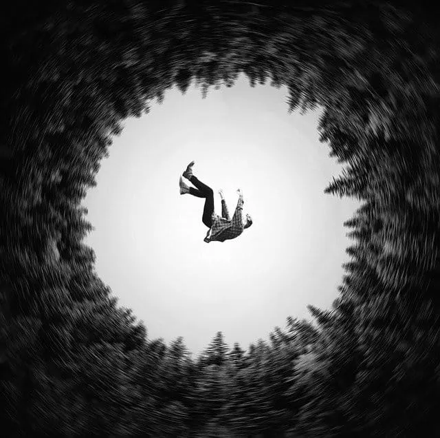 A person falling through a swirling black and white vortex surrounded by trees at the edge of a forest.