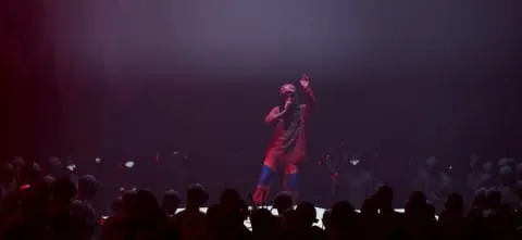 A performer on stage during a concert with dramatic lighting, engaging the audience.