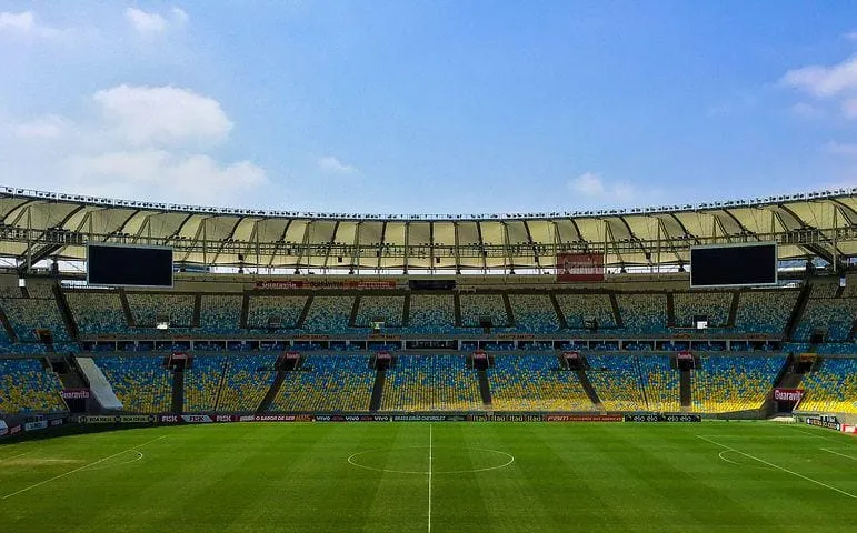 Bright stadium with colorful seats and a lush green soccer field, under a partly cloudy sky, showcasing the energetic atmosph