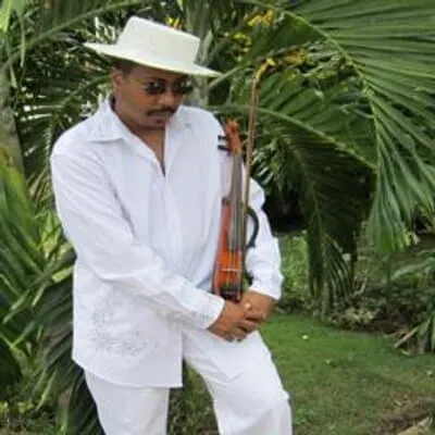 Man in white traditional attire holding a guitar in lush green tropical garden, wearing a wide-brimmed hat, representing musi