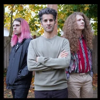Three young adults with distinct hairstyles standing outdoors in a park during autumn, showcasing diverse modern fashion and