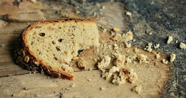 A partially eaten slice of bread with crumbs on a rustic wooden surface.