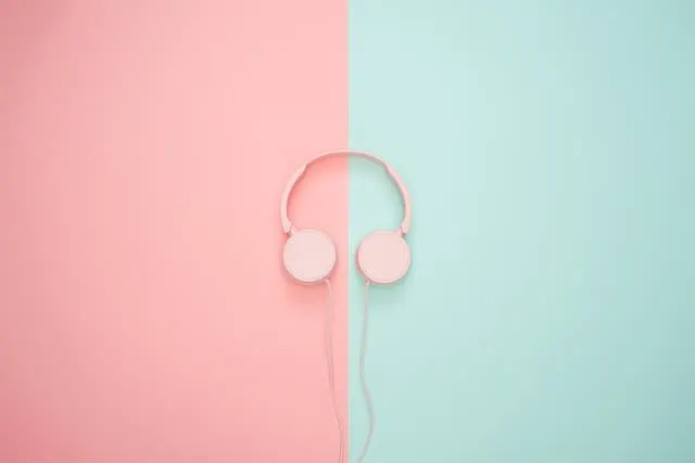 Pink and white headphones on a pastel split background, emphasizing music technology and digital media.