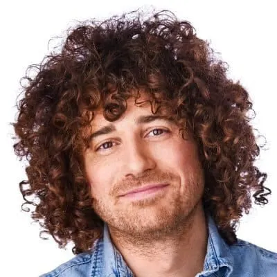 Vibrant curly-haired man smiling, close-up portrait, emphasizing diversity and personality in creative media and music indust