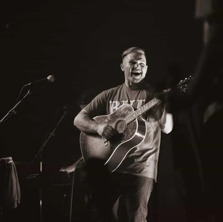 Excited male musician performing live with acoustic guitar on stage at concert, engaging audience, black and white concert im