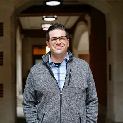 Bright smiling man wearing glasses and a gray jacket in a professional setting, capturing a confident and approachable vibe f