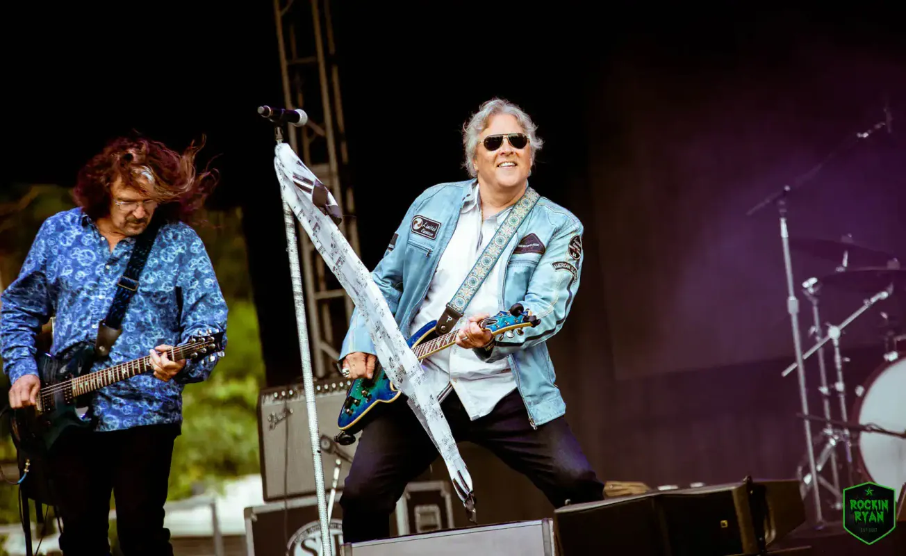Dynamic live music performance at a festival, featuring two guitarists playing passionately on stage with vibrant lighting an