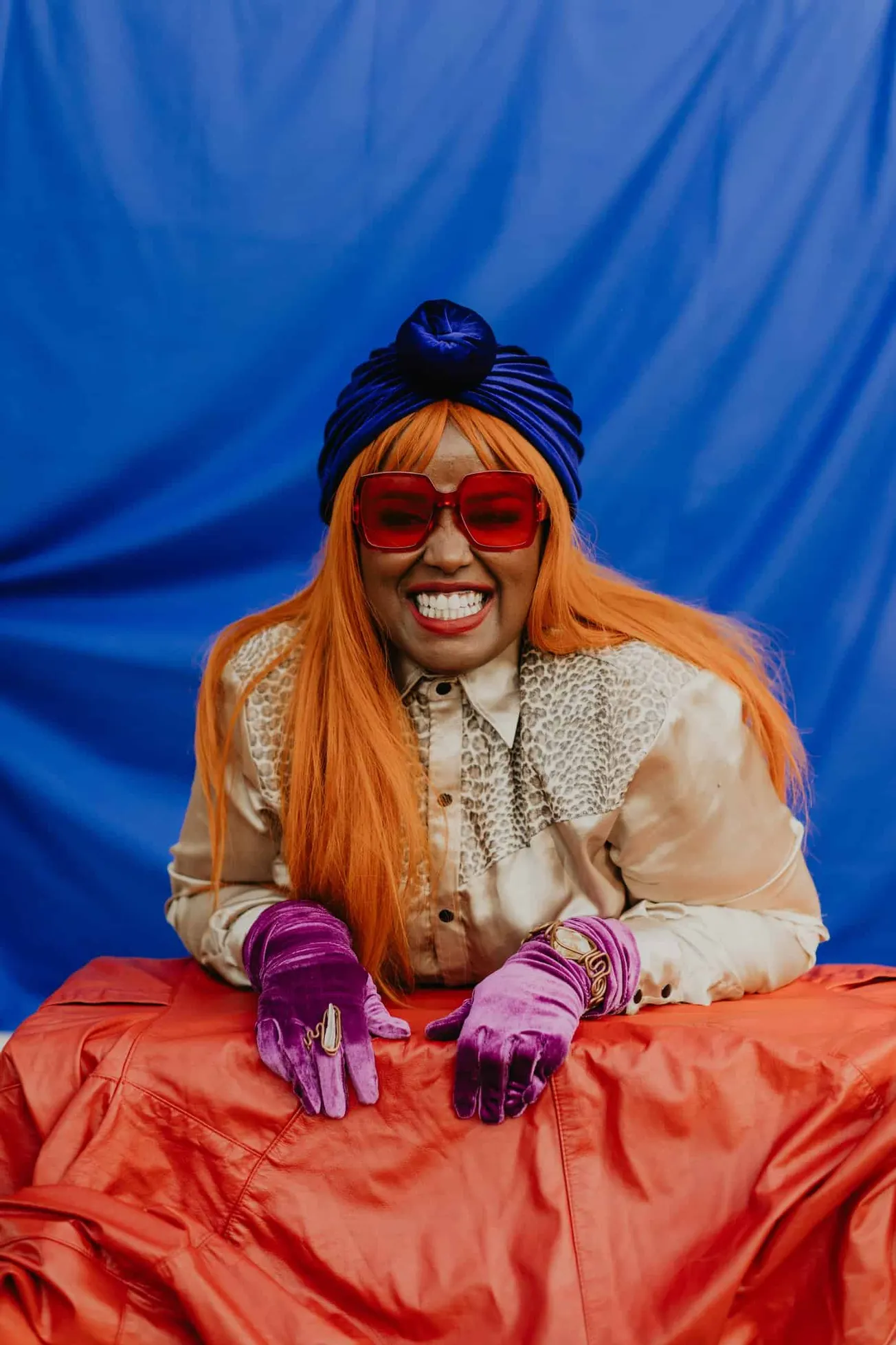 Colorful fashionable woman with bright orange hair, oversized red sunglasses, purple velvet gloves, bold accessories, stylish