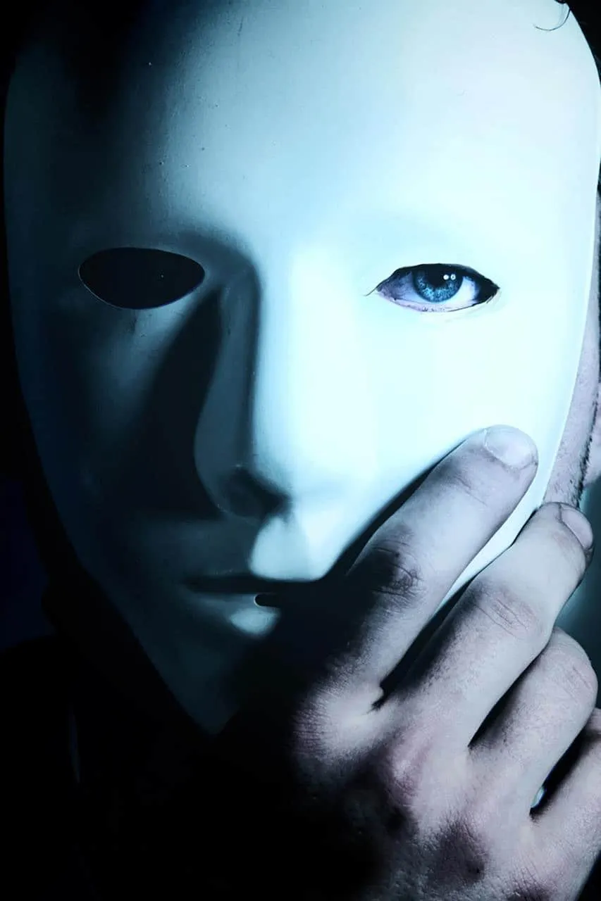 A person holding a white mask with a single blue eye visible, representing anonymity, digital identity, and privacy themes in