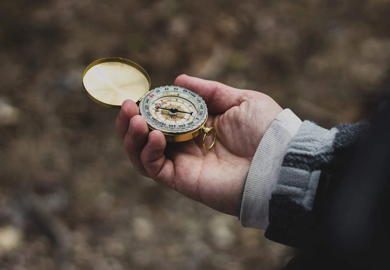 Compass held by a person outdoors, symbolizing navigation and direction.