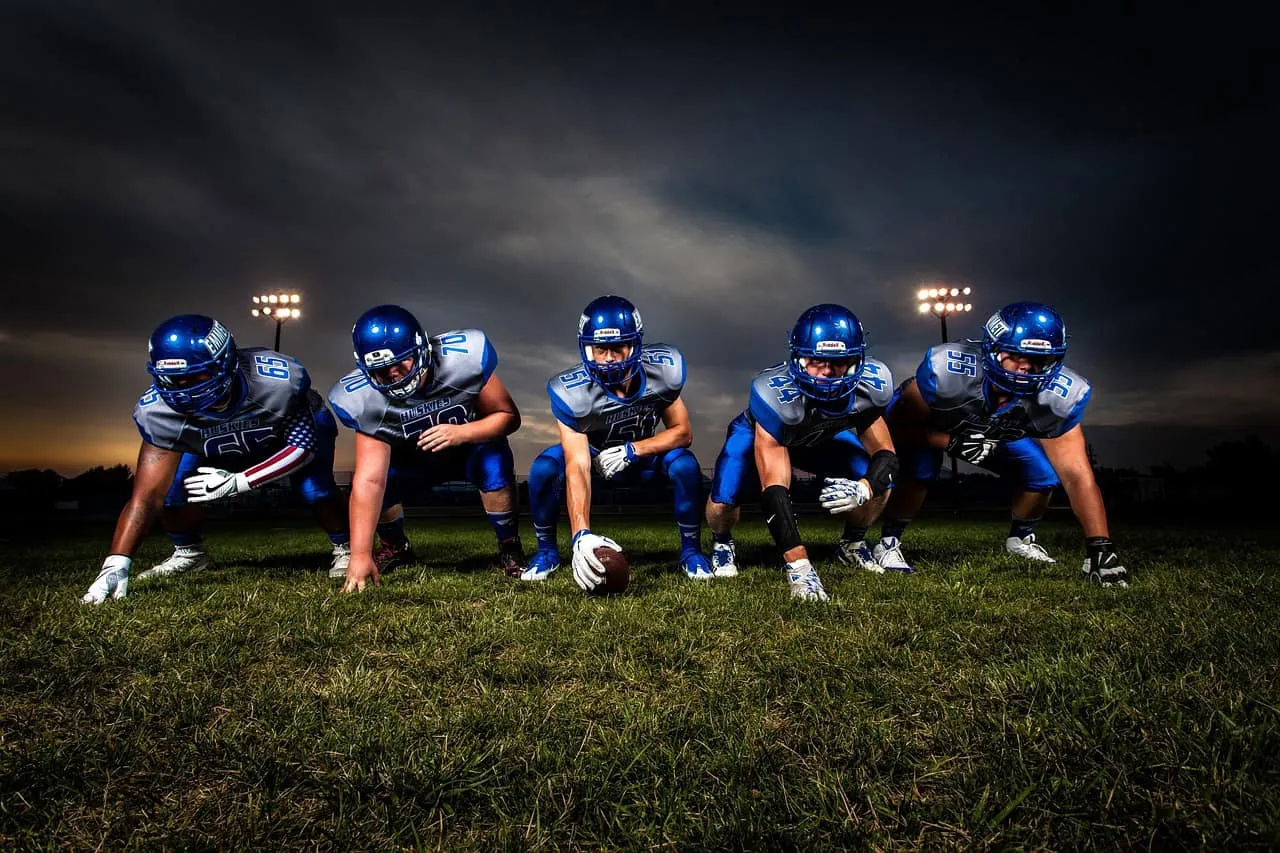 Team of American football players in blue uniforms preparing for game on a grassy field under evening sky.