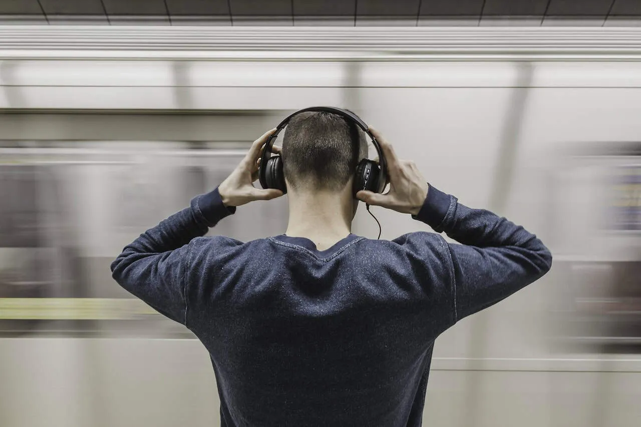 Headphones-wearing-man-on-subway-platform-listening-to-music-in-an-urban-setting-with-motion-blur-background.
