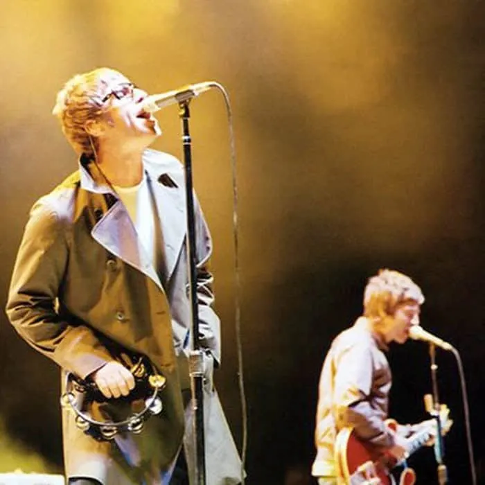 A musician singing into a microphone while holding a tambourine during a live performance on stage with yellow lighting atmos