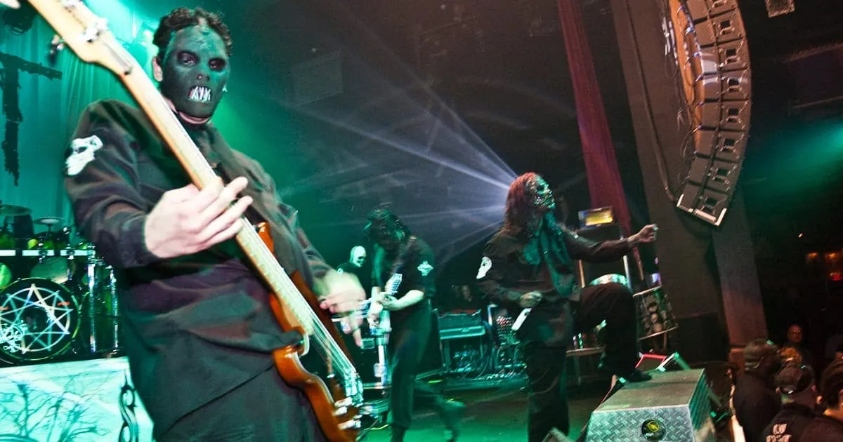 Dark masked guitarist performing live at a concert with dramatic lighting and stage effects, capturing the energy of a heavy