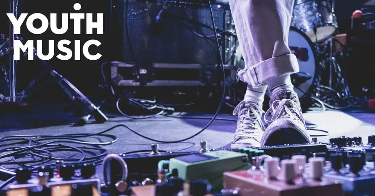 Performing youth musician on stage with guitar effects pedals and sound equipment, emphasizing youth music, live performance,